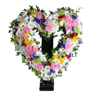 Hjärtformad blomsterkrans med rosor i rosa, röda och gula färger, blandade med vita och blå blommor samt gröna blad.