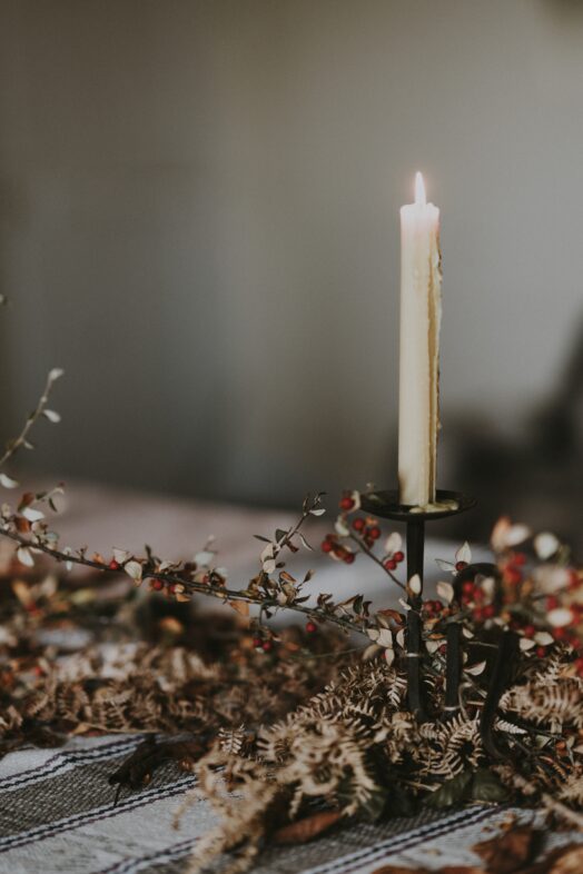 Ett tänt ljus står i en ljusstake omgiven av torkade blommor.