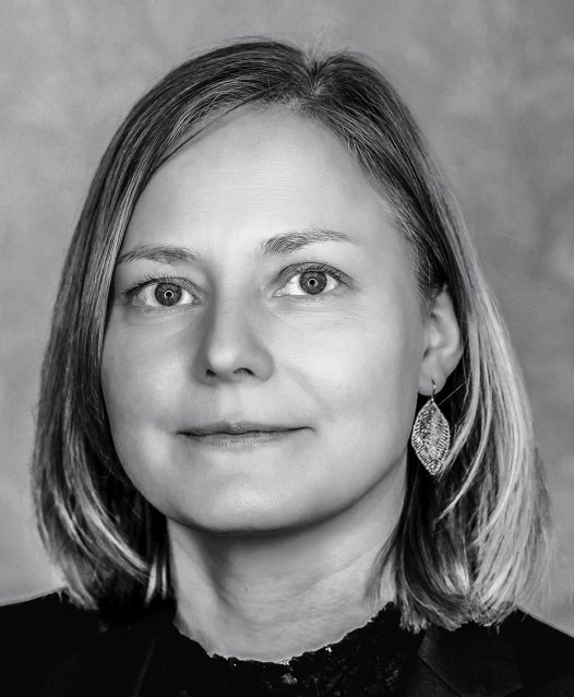 Kvinna med axellångt hår och stora örhängen ser in i kameran. Bilden är i svartvitt.