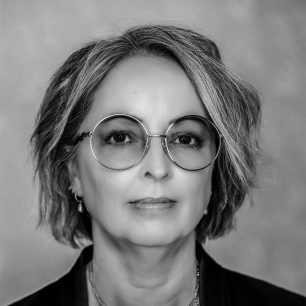 Kvinna med kort hår och runda glasögon, ser rakt fram i en svartvit porträttbild.